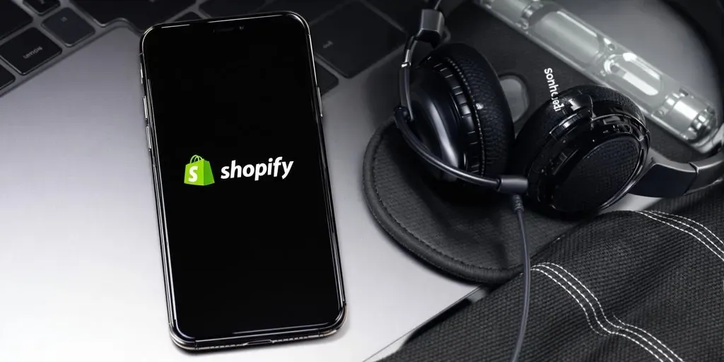Smartphone with Shopify logo and headset on table.